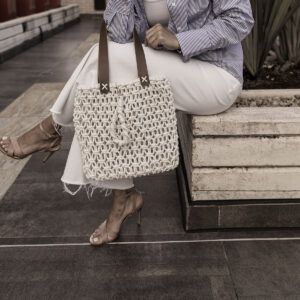 Mulher segurando bolsa de macramê branca modelo Brisa, mostrando a textura sofisticada dos nós.